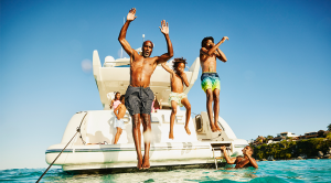 Wide shot father and sons jumping into water from swim deck of yacht